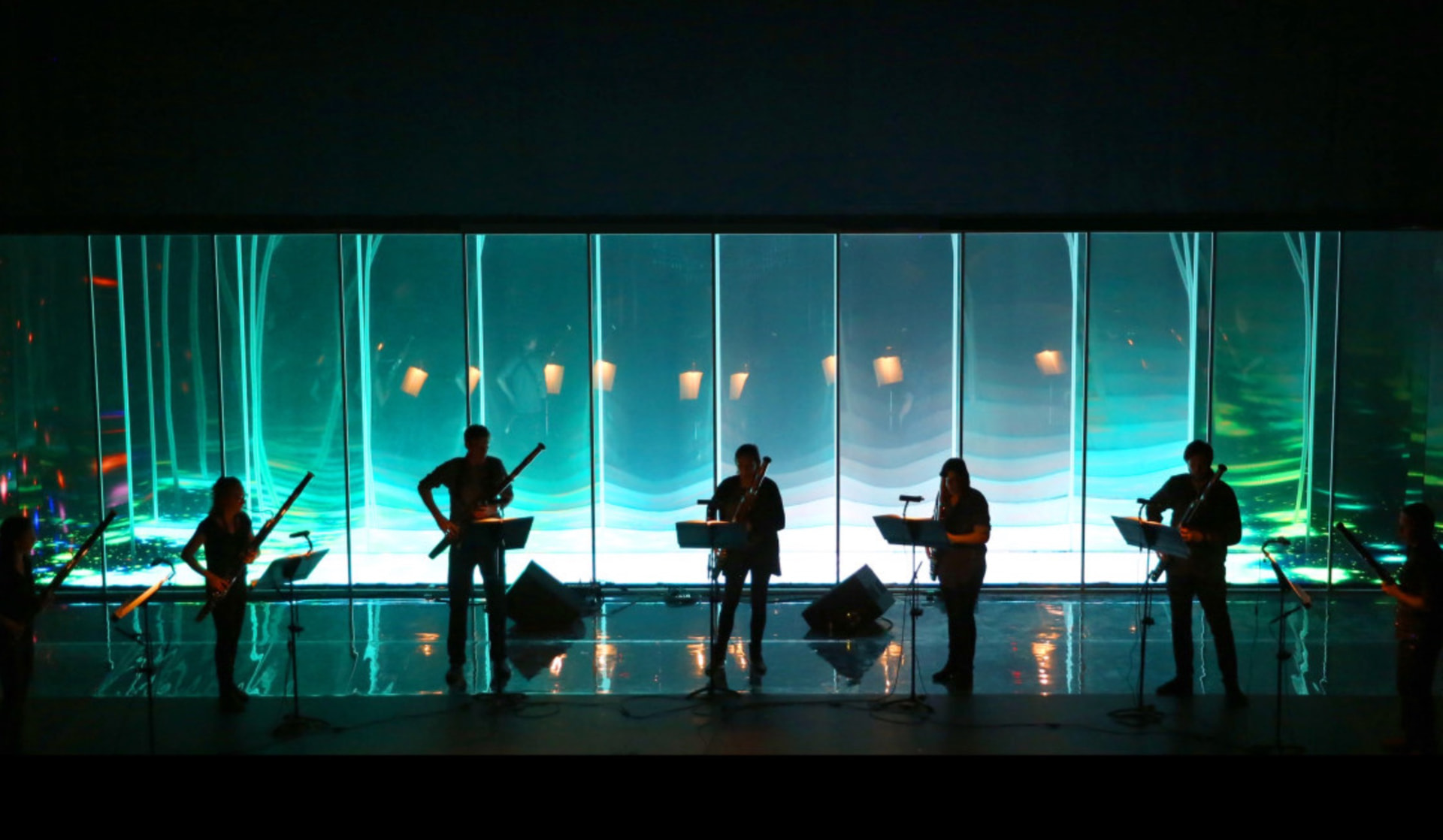 Bassoon ensemble performing in front of a large green and turquoise projection