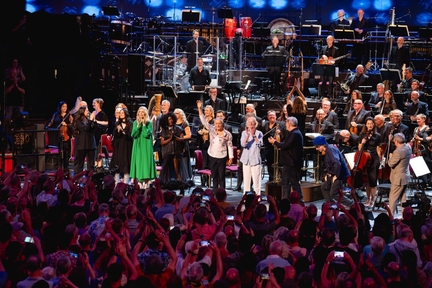 Performers and orchestra taking a curtain call before a cheering audience